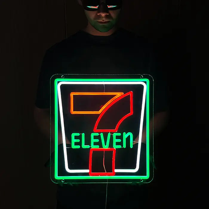 7-Eleven Neon LED Schild wird im abgedunkelten Raum vor dem Körper gehalten, Ziffer und Schriftzug leuchten