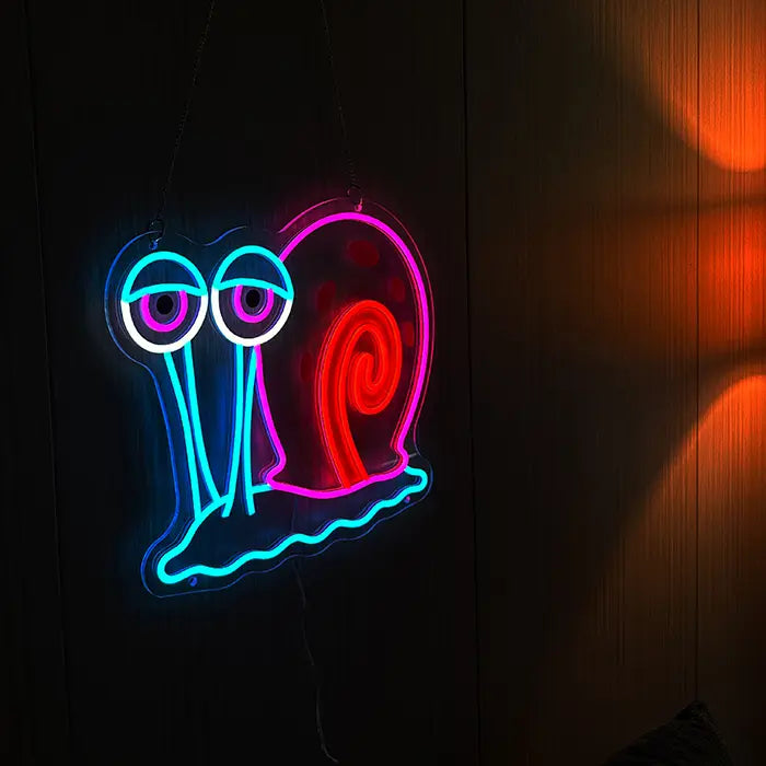 Gary Schnecke Neon LED Schild an dunkler Holzwand hängend, daneben warmes Licht einer Lampe