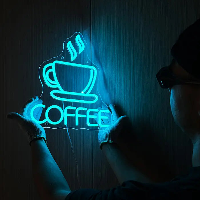 Coffee Tasse Neon LED Schild wird an der Wand ausgerichtet, eine Person mit Handschuhen hält es fest