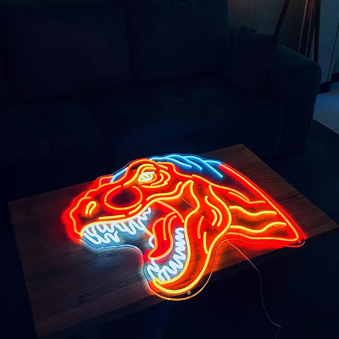 T-Rex Dino Neon LED Schild liegend auf einem Holztisch vor einem Sofa, rot und orange leuchtend