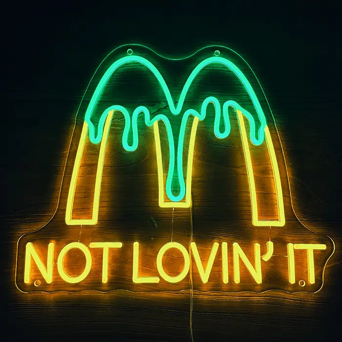 McDonald's Not Lovin' It Neon LED Schild frontal an dunkler Wand, gelbes M mit grünem Tropf-Effekt über dem Schriftzug