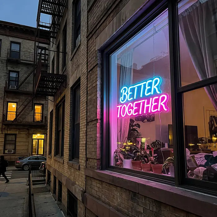 Better Together Neon LED Schild in Blau-Pink im Fenster eines Backsteinhauses, von der Straße aus gesehen