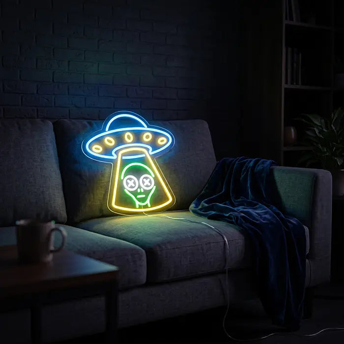 UFO Alien Entführung Neon LED Schild auf einem grauen Sofa aufgestellt, daneben Decke und Tasse