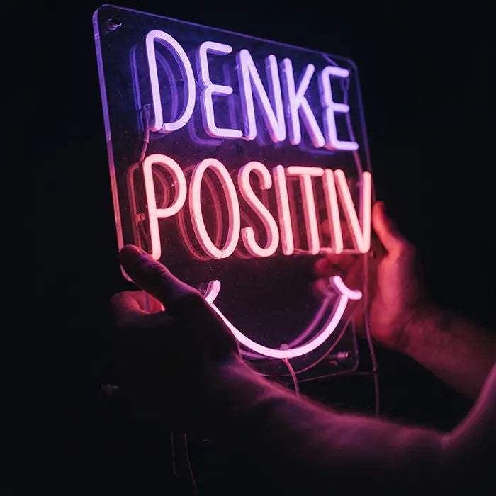 Denke Positiv Neon LED Schild schräg in zwei Händen, klare Acrylplatte und Kabelführung gut sichtbar