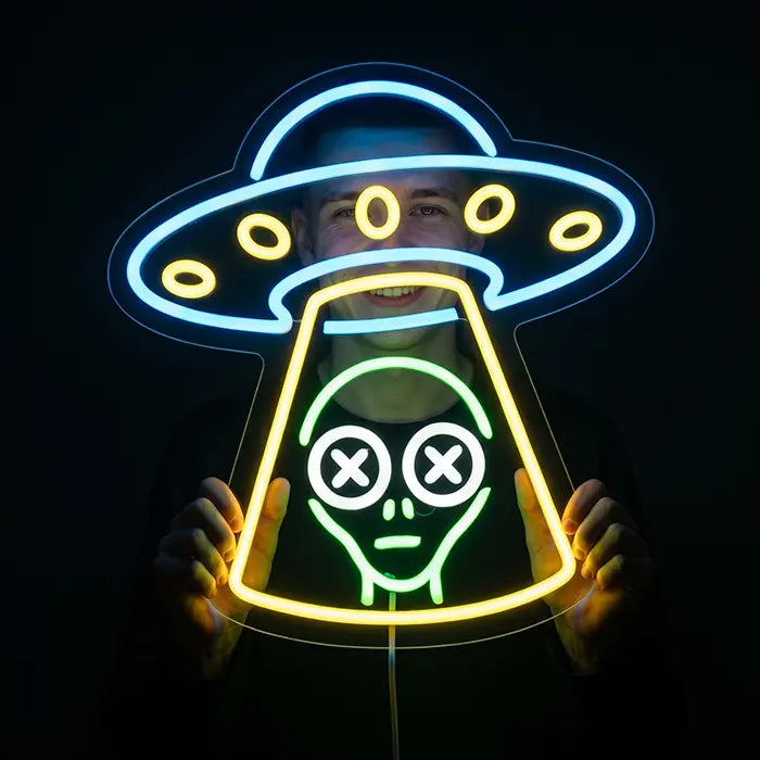 UFO Alien Entführung Neon LED Schild wird mit beiden Händen vor das Gesicht gehalten, gelber Lichtkegel leuchtet