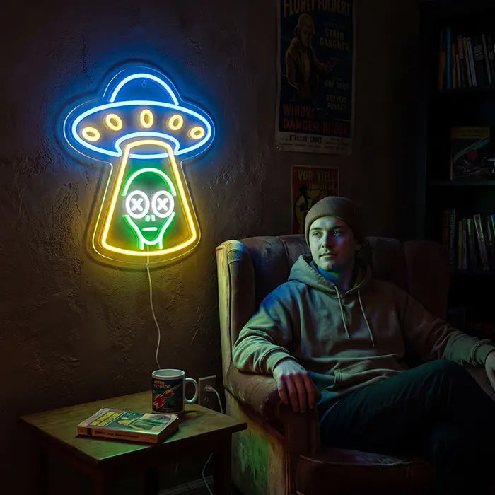 UFO Alien Entführung Neon LED Schild an der Wand neben einer Person mit Mütze, die entspannt im Sessel sitzt