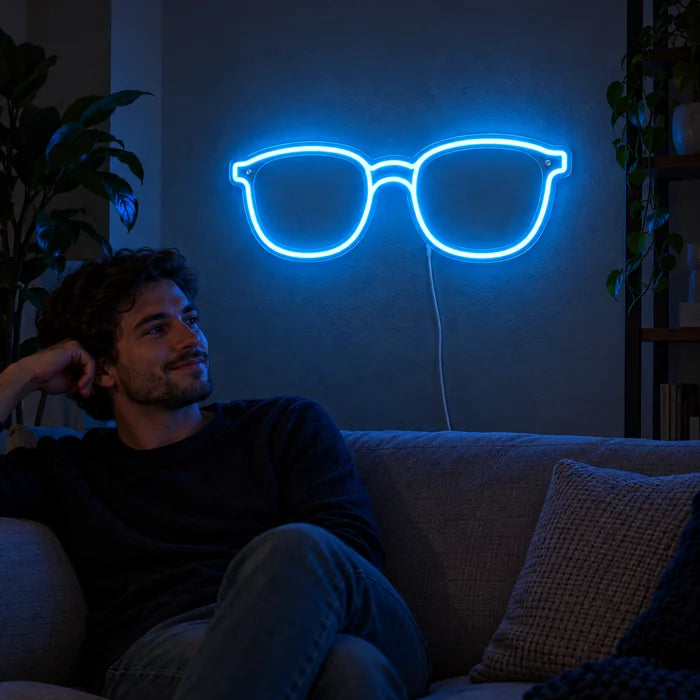 Blaue Brille Neon LED Schild an der Wohnzimmerwand, davor entspannt eine Person auf dem Sofa