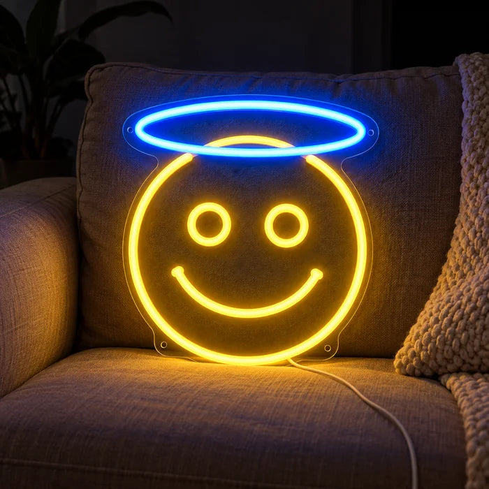 Engel-Smiley Neon LED Schild auf einem gemütlichen Sofa zwischen Kissen und Decke