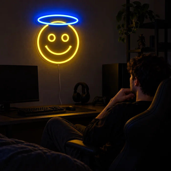 Engel-Smiley Neon LED Schild über dem Gaming-Schreibtisch, davor ein Spieler im Gaming-Stuhl