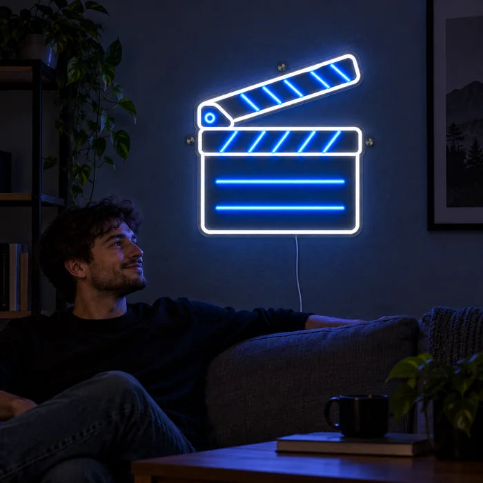 Filmklappe Neon LED Schild an der Wohnzimmerwand, davor entspannt eine Person auf dem Sofa