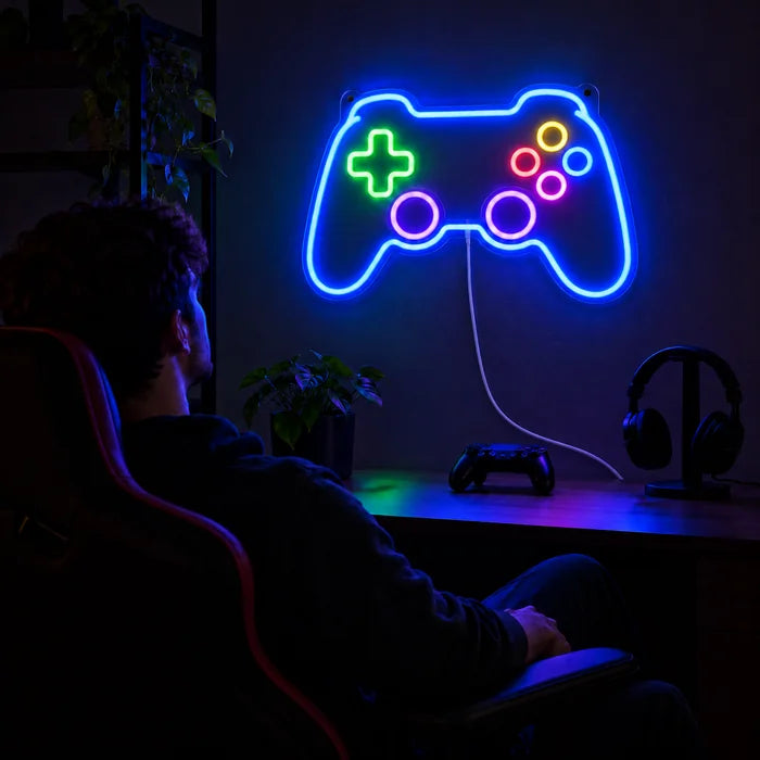 Gamecontroller Neon LED Schild über dem Gaming-Schreibtisch, davor ein Spieler im Gaming-Stuhl