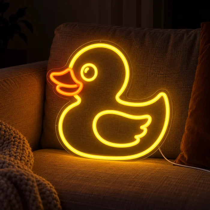 Gelbe Ente Neon LED Schild auf einem gemütlichen Sofa zwischen Kissen und Decke
