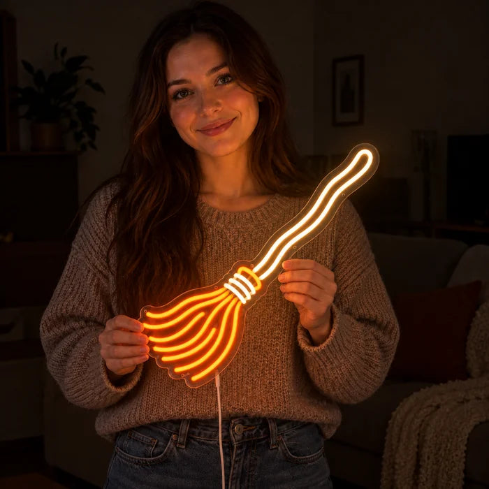 Hexenbesen Neon LED Schild in den Händen einer lächelnden Frau vor dunklem Hintergrund