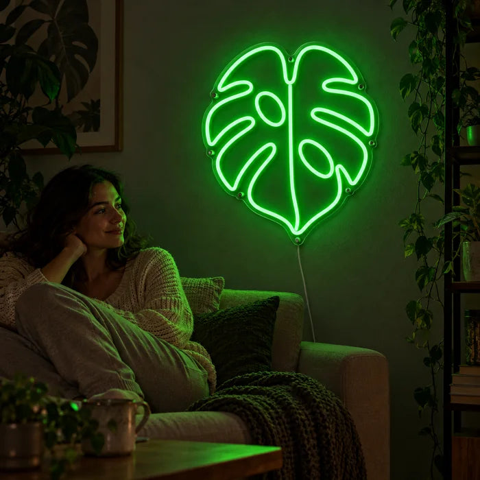Monstera Neon LED Schild an der Wohnzimmerwand, davor entspannt eine Person auf dem Sofa