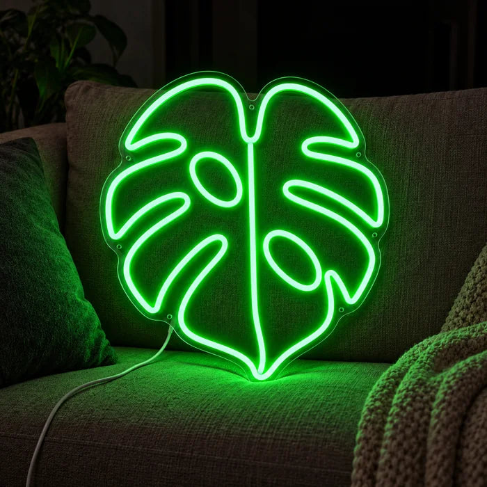 Monstera Neon LED Schild auf einem gemütlichen Sofa zwischen Kissen und Decke