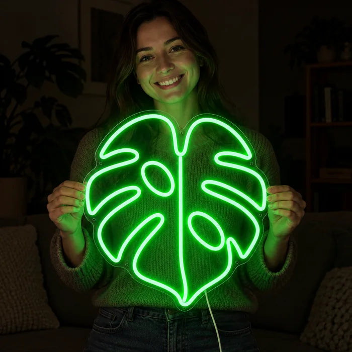 Monstera Neon LED Schild in den Händen einer lächelnden Frau vor dunklem Hintergrund