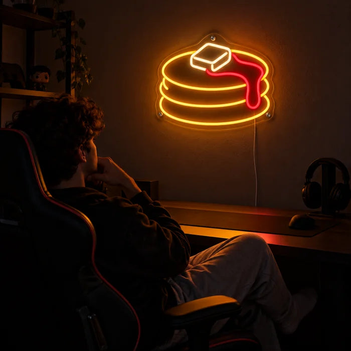 Pfannkuchen Neon LED Schild über dem Gaming-Schreibtisch, davor ein Spieler im Gaming-Stuhl