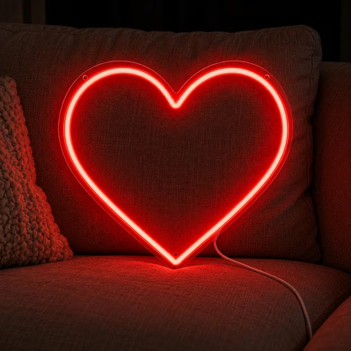 Rotes Herz Neon LED Schild auf einem gemütlichen Sofa zwischen Kissen und Decke