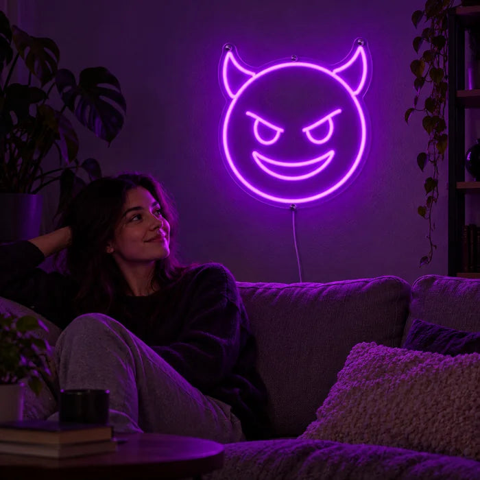 Teufelsgrinsen Neon LED Schild an der Wohnzimmerwand, davor entspannt eine Person auf dem Sofa