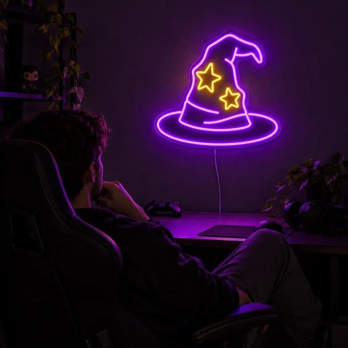 Zauberhut Neon LED Schild über dem Gaming-Schreibtisch, davor ein Spieler im Gaming-Stuhl