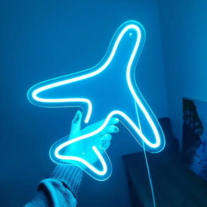 Flugzeug Neon LED Schild in Blau, aus der Nähe in der Hand gehalten vor einer hell angestrahlten Wand