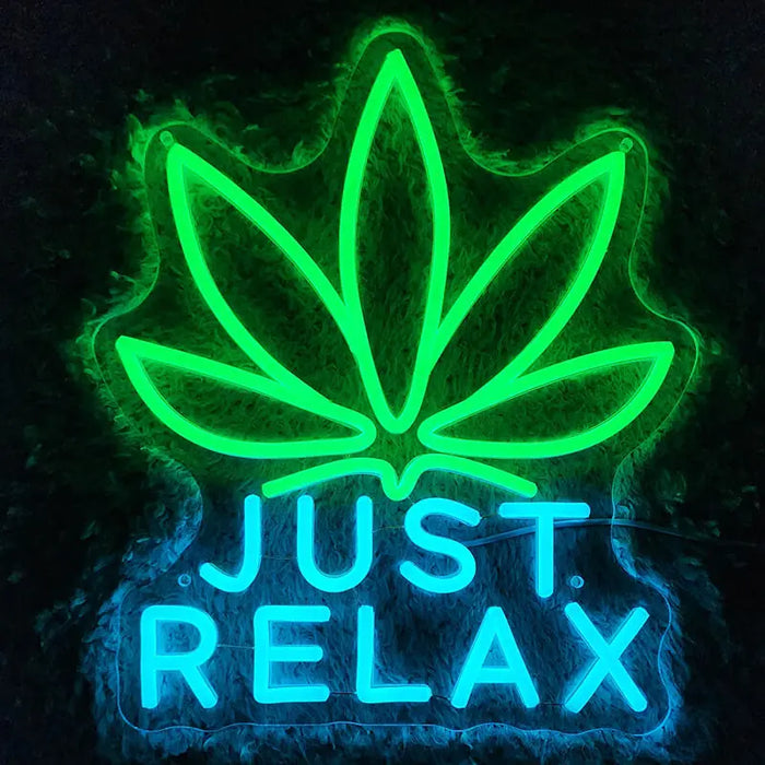 Just Relax Neon LED Schild mit grün leuchtendem Hanfblatt über dem blauen Schriftzug an dunkler Wand