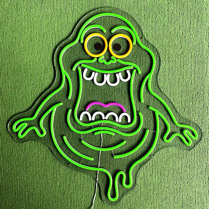Schleimgeist Neon LED Schild ausgeschaltet vor grüner Wand, klare Acrylkontur mit orangen Augenringen und weißen Zähnen