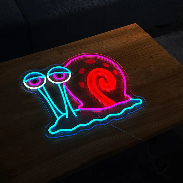 Gary Schnecke Neon LED Schild auf einem Holztisch stehend, dahinter ein Sofa im dunklen Raum
