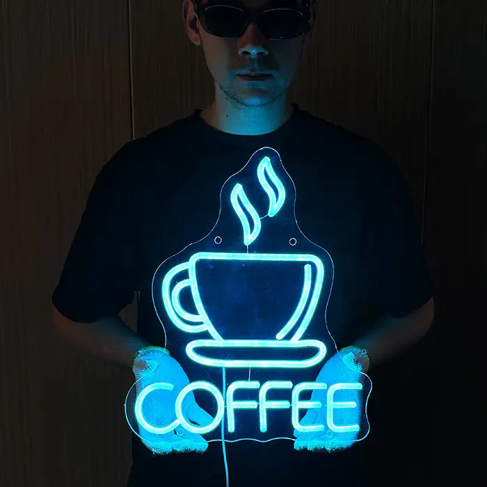 Coffee Tasse Neon LED Schild wird mit beiden Händen vor den Körper gehalten, Eisblau leuchtend
