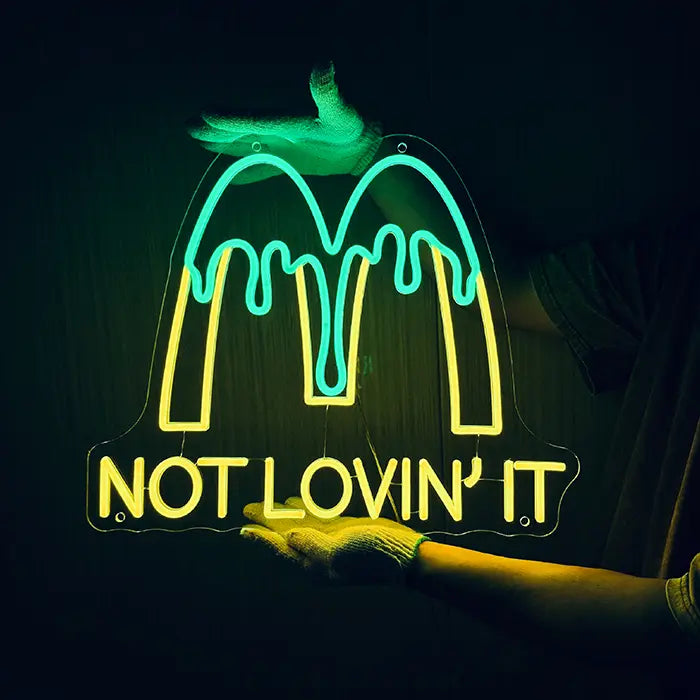McDonald's Not Lovin' It Neon LED Schild wird mit Handschuhen an eine dunkle Wand gehalten