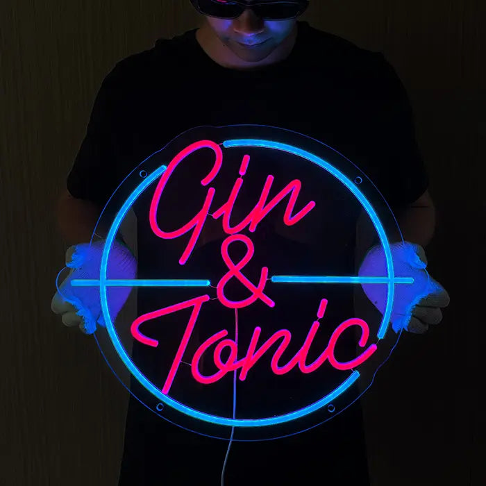 Gin & Tonic Neon LED Schild wird mit Handschuhen vor den Körper gehalten, pinker Schriftzug im türkisen Kreis