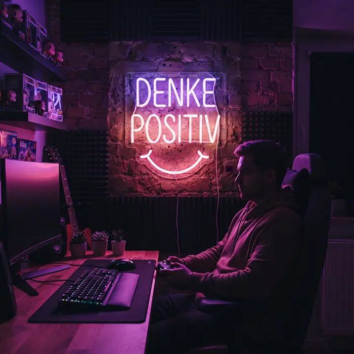 Denke Positiv Neon LED Schild über dem Gaming-Setup eines Spielers mit Monitor, Tastatur und Controller