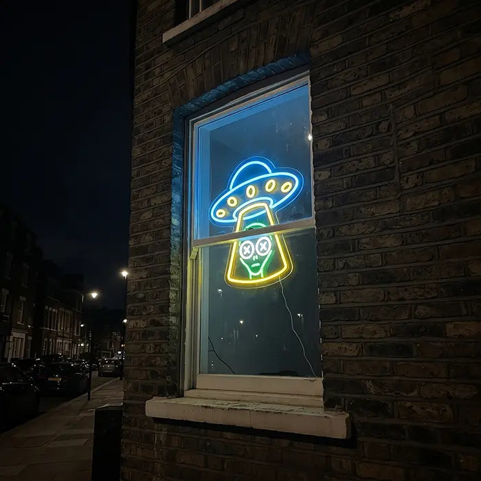 UFO Alien Entführung Neon LED Schild im Fenster eines Backsteinhauses, nachts von der Straße aus gesehen
