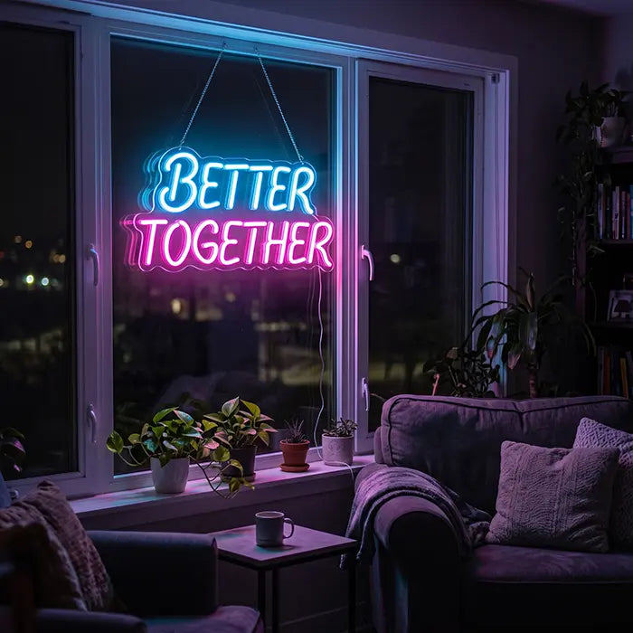 Better Together Neon LED Schild in Blau-Pink in einem Fenster mit Pflanzen, davor ein Sofa