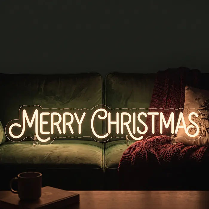 Merry Christmas Neon LED Schild auf einem Sofa vor Kissen und Wolldecke aufgestellt