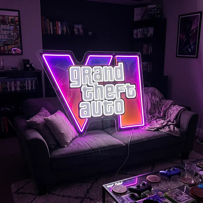 GTA VI Logo Neon LED Schild mit UV-Druck über einem grauen Sofa, davor ein Couchtisch mit Controllern