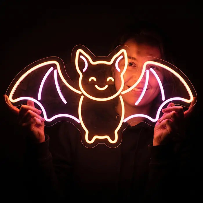 Fledermaus Neon LED Schild wird von einer lächelnden Frau im dunklen Raum vor sich gehalten
