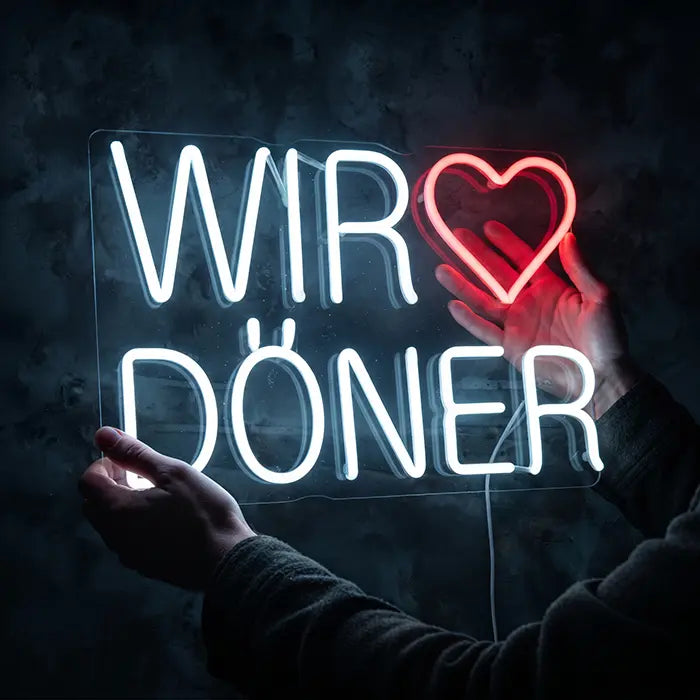 Wir lieben Döner Neon LED Schild wird mit der Hand vor dunklem Hintergrund gehalten, Herz leuchtet rot
