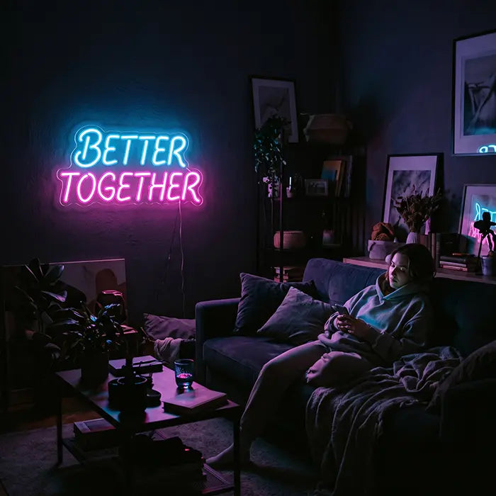 Better Together Neon LED Schild in Blau-Pink über einem Sofa, darauf eine Frau mit Handy