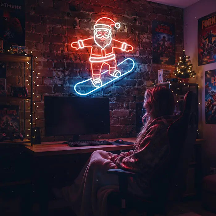 Weihnachtsmann mit Snowboard Neon LED Schild über einem Gaming-Schreibtisch, davor eine Person im Stuhl, daneben ein Weihnachtsbaum