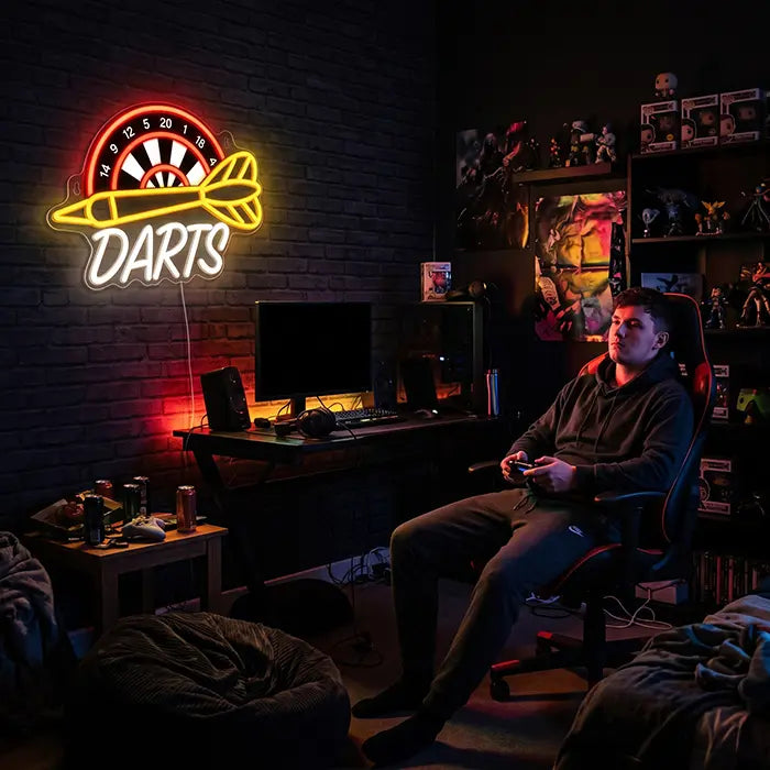 Darts Neon LED Schild mit UV-Druck an einer Backsteinwand im Gaming-Zimmer, davor ein Mann mit Controller im Gaming-Stuhl