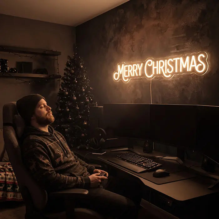 Merry Christmas Neon LED Schild über einem Schreibtisch, davor eine Person im Gaming-Stuhl neben einem Weihnachtsbaum