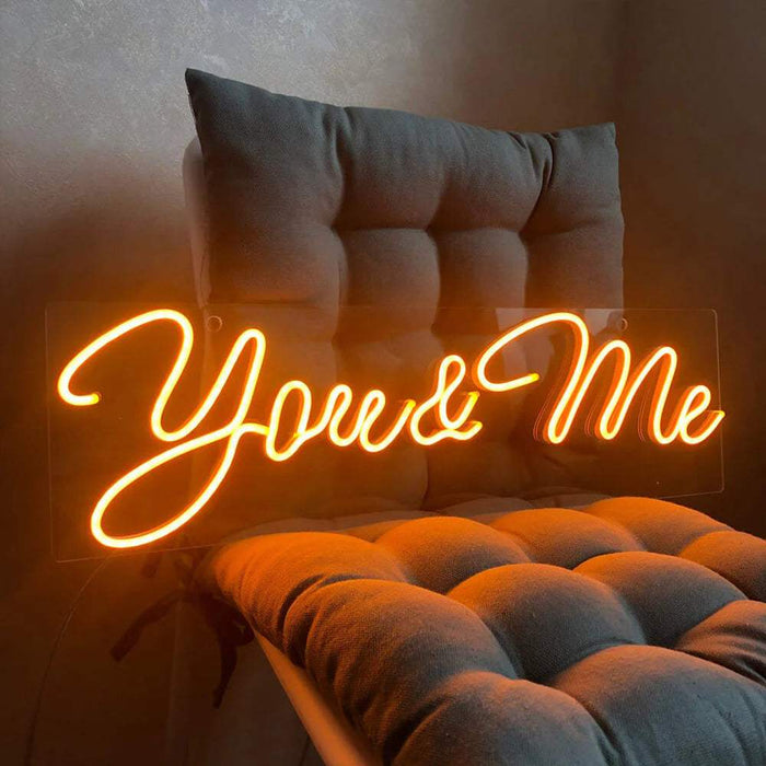 You & Me Neon LED Schild in orange leuchtender Schreibschrift auf klarer Acrylplatte vor einer Wand
