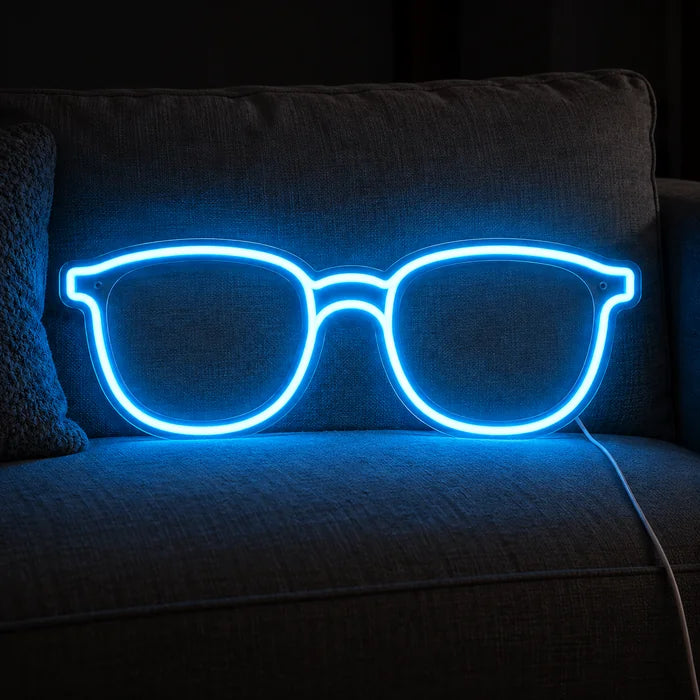 Blaue Brille Neon LED Schild auf einem gemütlichen Sofa zwischen Kissen und Decke