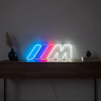 Leuchtreklame in der Form des BMW M Serienlogos, die in einem Raum auf einem Holzschrank platziert ist und als Racing-Dekoration dient