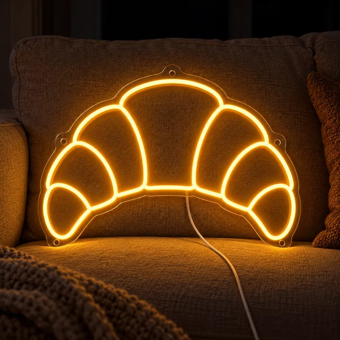 Buttercroissant Neon LED Schild auf einem gemütlichen Sofa zwischen Kissen und Decke