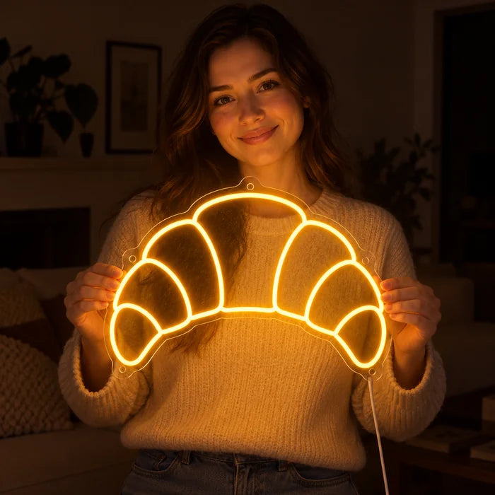 Buttercroissant Neon LED Schild in den Händen einer lächelnden Frau vor dunklem Hintergrund