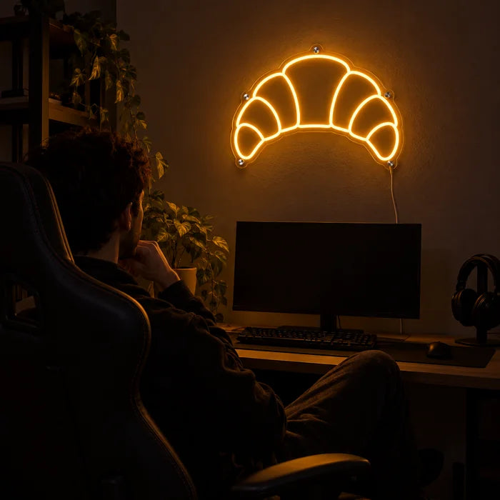 Buttercroissant Neon LED Schild über dem Gaming-Schreibtisch, davor ein Spieler im Gaming-Stuhl