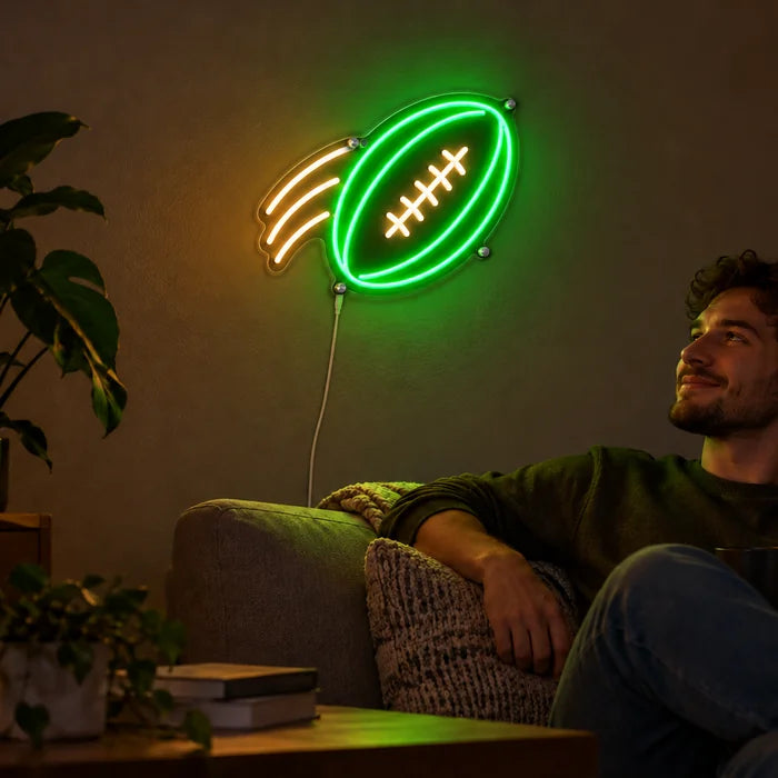 Football im Flug Neon LED Schild an der Wohnzimmerwand, davor entspannt eine Person auf dem Sofa