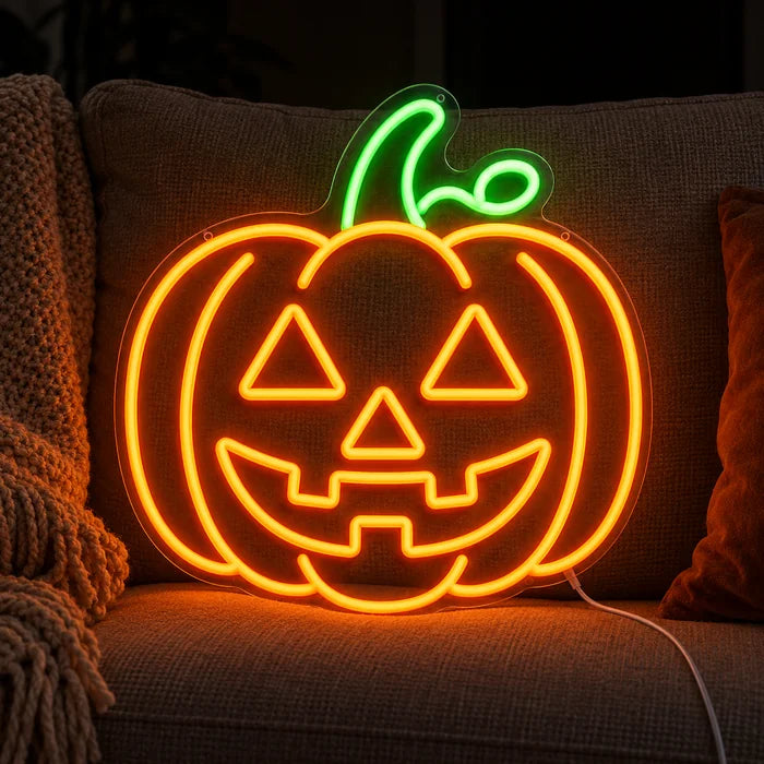 Halloween-Kürbis Neon LED Schild auf einem gemütlichen Sofa zwischen Kissen und Decke